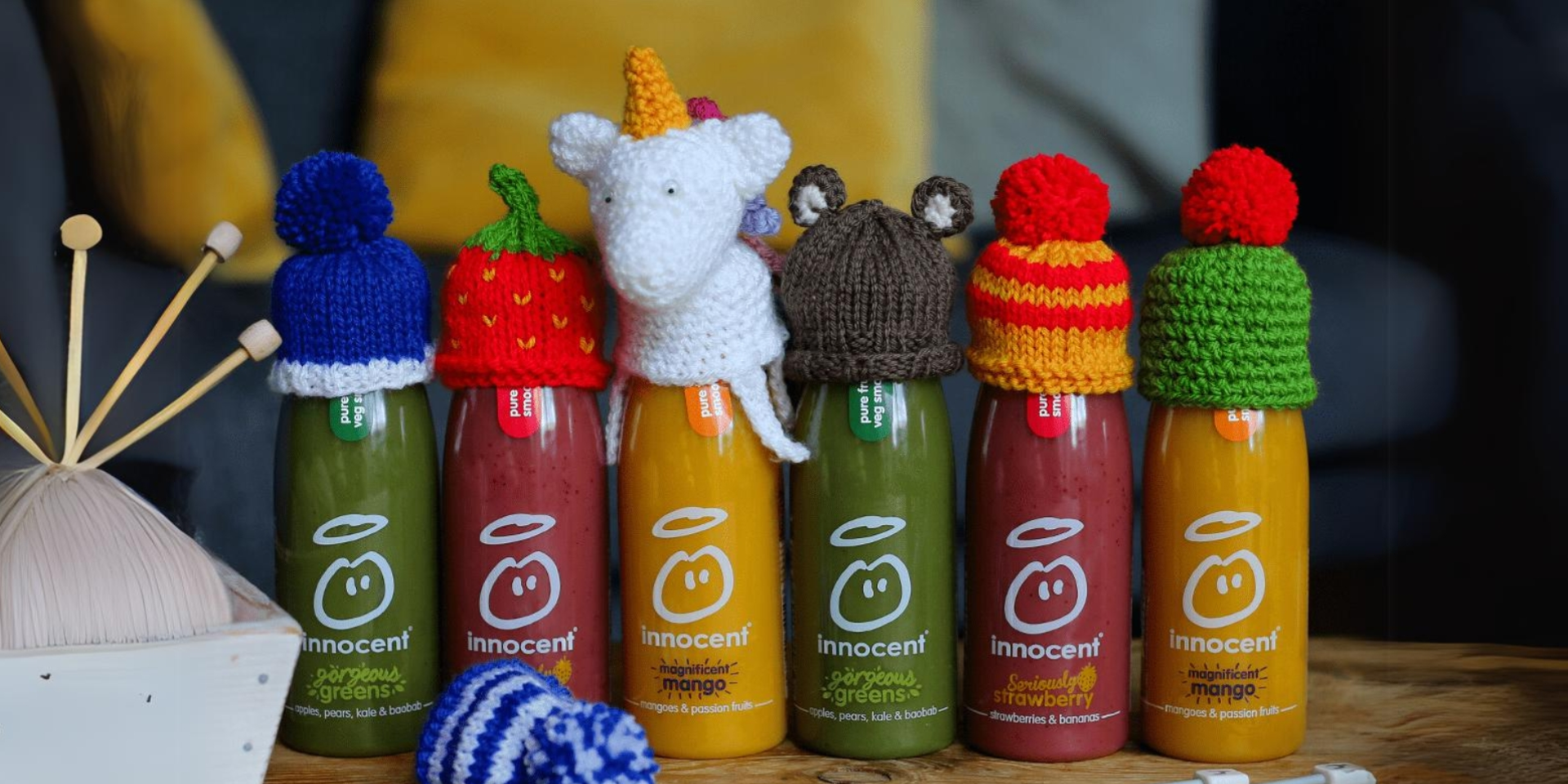 6 smoothie bottles wearing small knitted hats stood on a table. 
