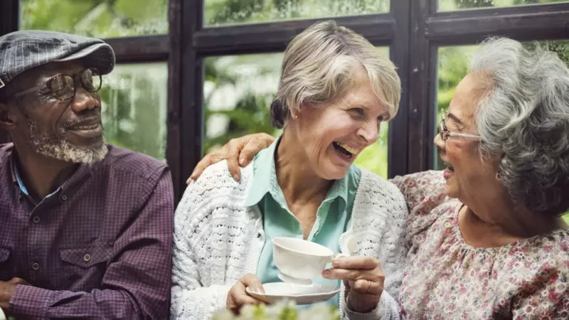Three older people laughing indoors. 